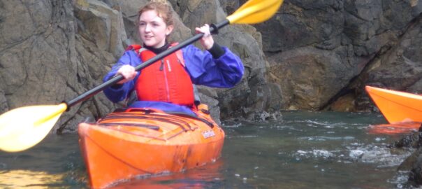 Beginner learning sea kayaking skills with a coach in Pembrokeshire.