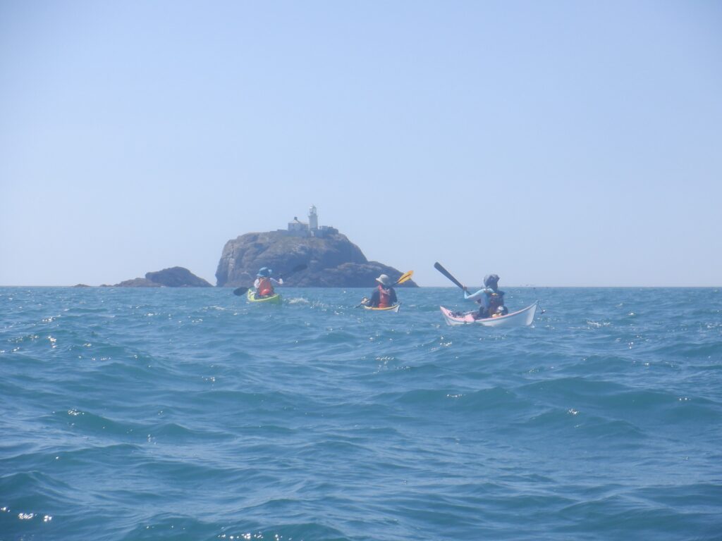 Sea kayakers crossing open water towards an offshore Pembrokeshire island